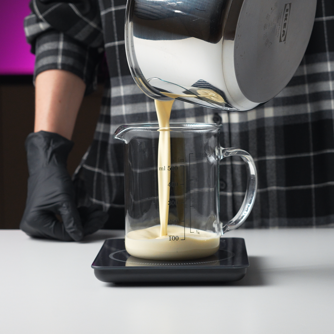 Heavy cream being poured into a measuring bowl on a digital kitchen scale to measure its weight.
